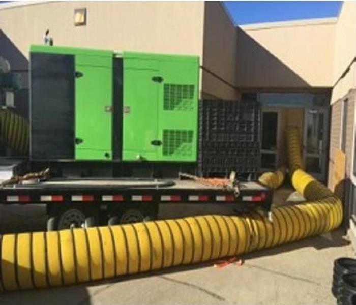 Green large loss desiccant with yellow hoses running into a building.